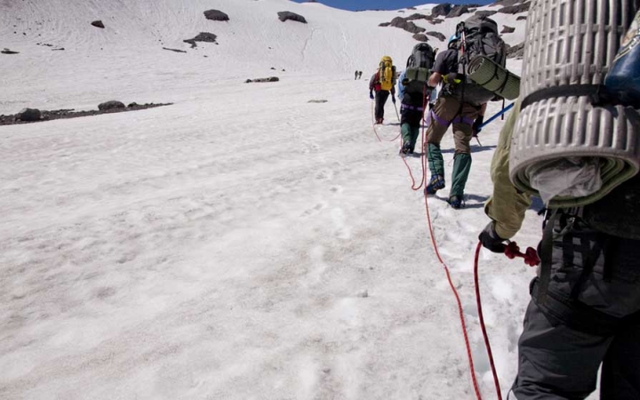 A group of people attached to each other by ropes make their way up a snowy incline.